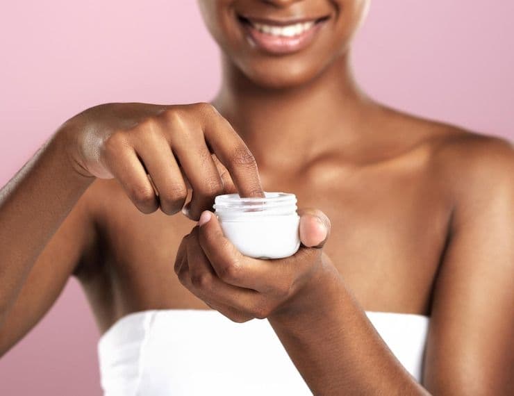 Woman applying skincare cream from a small white jar.